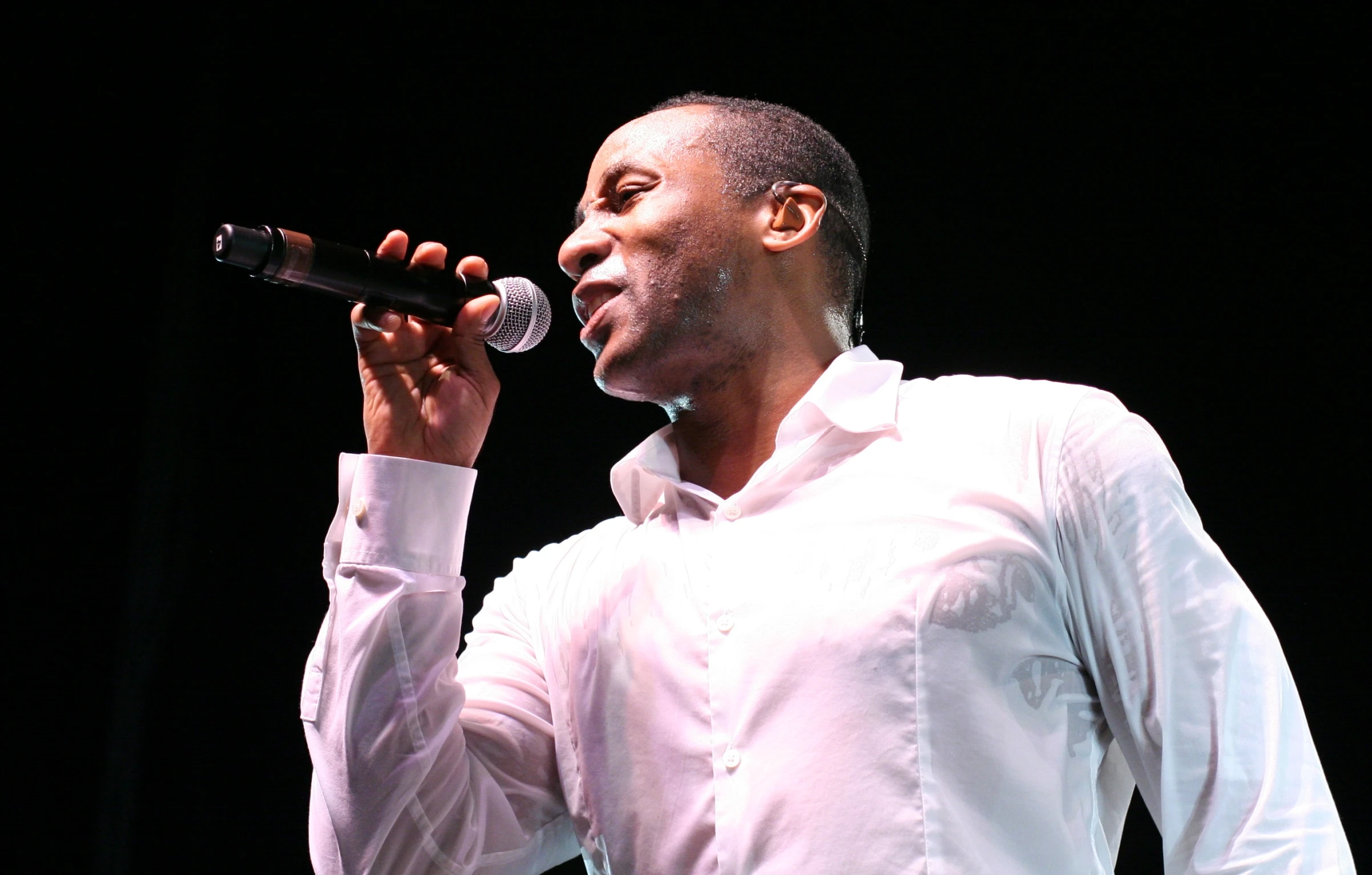 man singing into a microphone while wearing a white shirt