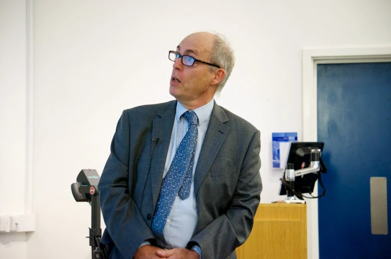 man with glasses on in room holding his hands in his pockets