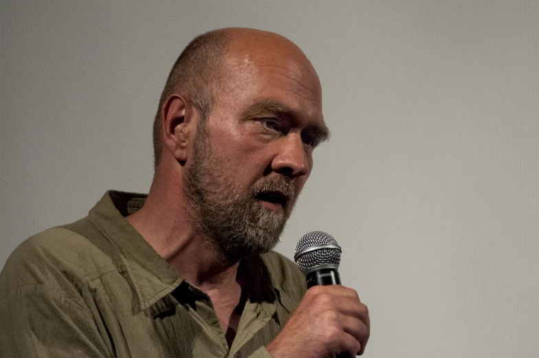 a man holding a microphone and wearing an army green shirt