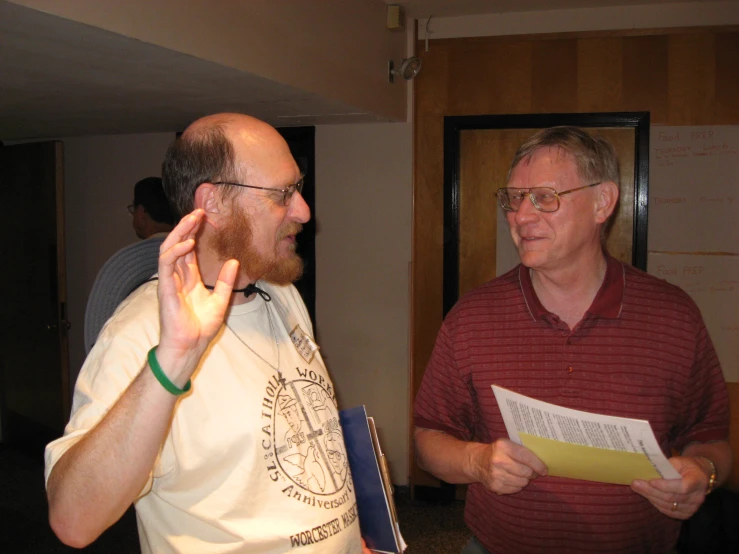 two men standing next to each other and looking at paperwork