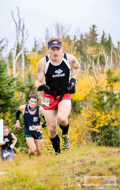 an athlete wearing all black running near another runner in the woods