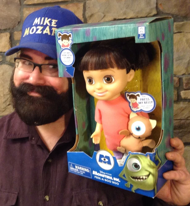 man with beard in hat holding up an in - box figure of mike e kotta