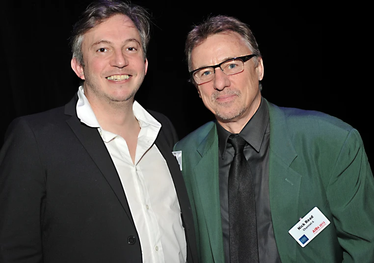 a man with glasses and a green jacket next to another man