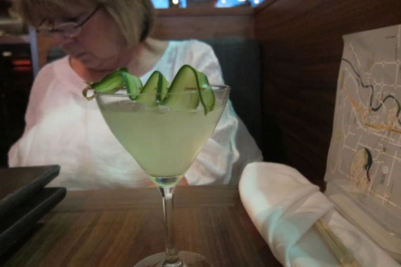 a woman sitting at a wooden table with a glass filled with green liquid