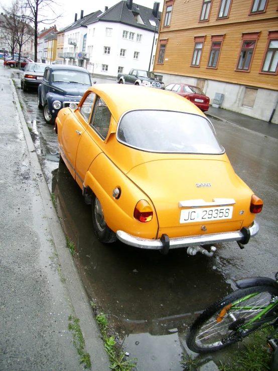 a very old yellow car parked in the rain