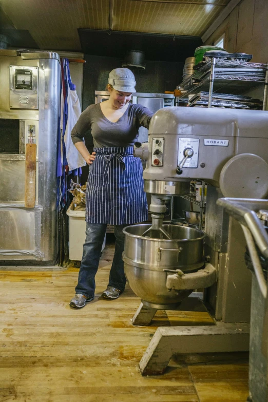a woman stands in a kitchen beside an industrial mixer