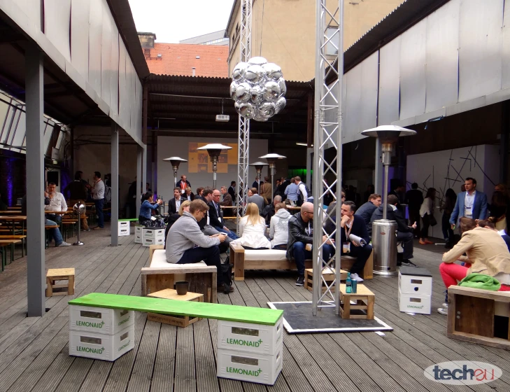 a crowd of people sit on chairs and tables in an open courtyard