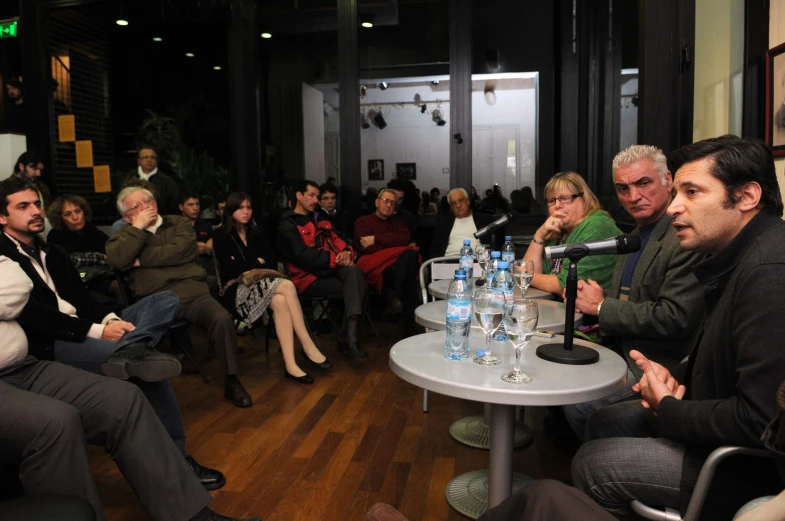 people sitting at tables drinking water and listening to the speakers