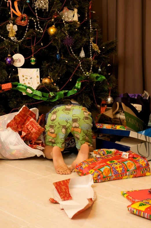 a small child on the floor looking at presents underneath the tree