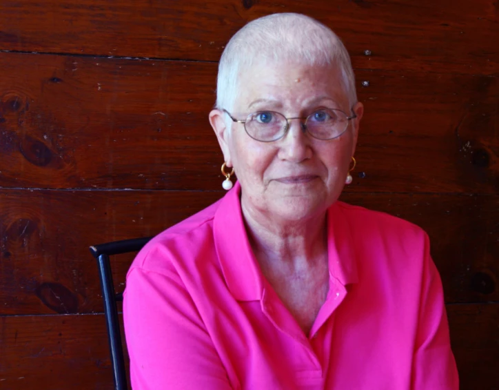 an older woman wearing glasses in front of a wooden wall