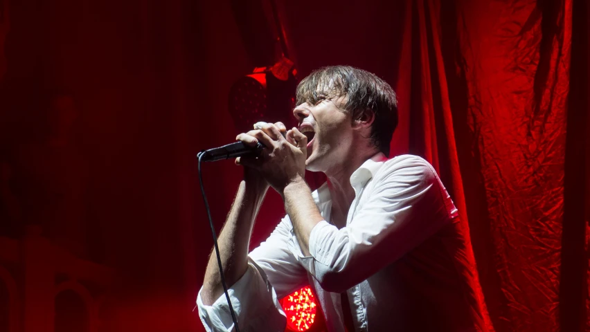 man in white shirt singing into a microphone on stage