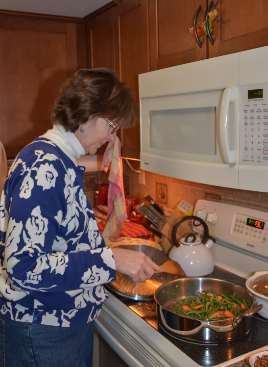 an older woman cooking in a kitchen near the stove