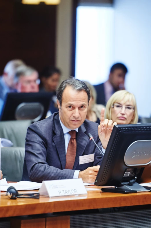 a man sits at a table with a monitor in front of him