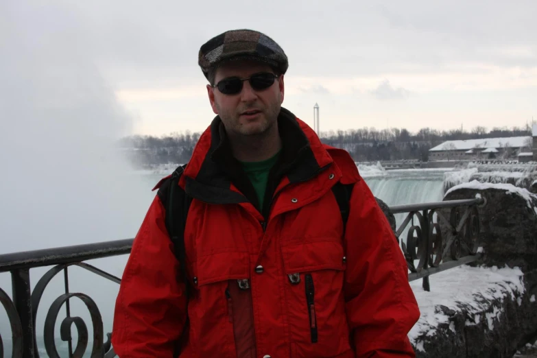 the man wearing the hat and jacket is standing in front of a bridge