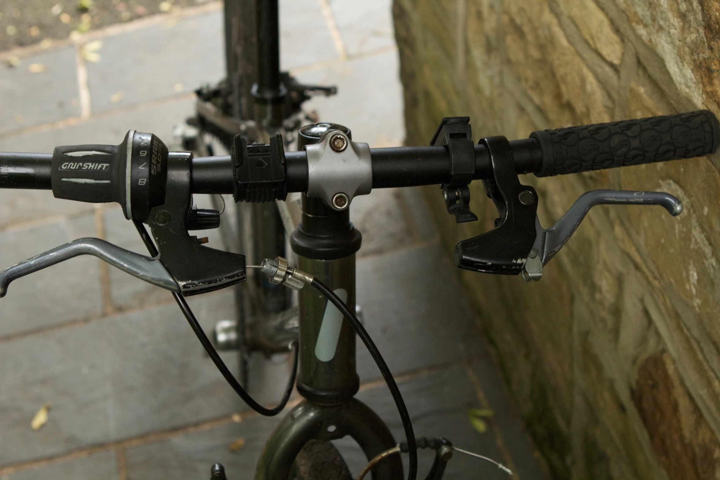 two black handlebars on a bike parked by a stone wall