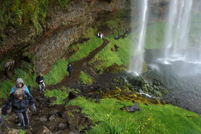 many people are walking down the hill to get in front of the waterfall