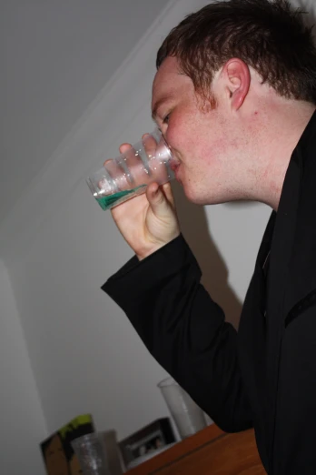 a man drinking from a glass that is sitting on top of the table