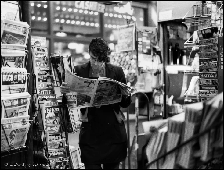 a woman reads a newspaper while standing by a store