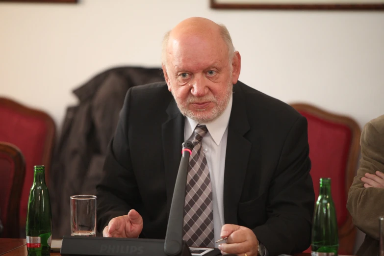 the older man in black suit and tie is holding a drink