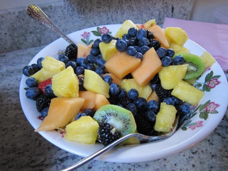 a fruit salad with cut pineapples, kiwi, blueberries and raspberries