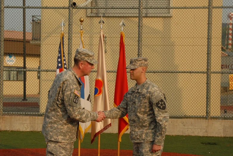 two men shake hands in front of flags