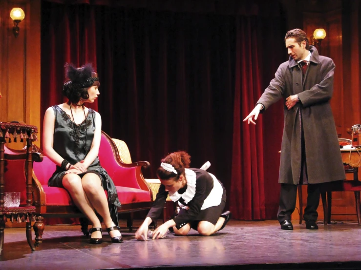 a man in a black suit is standing next to a lady on a red chair