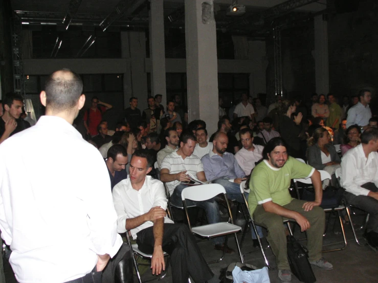 a crowd of people sitting in a room with a man talking on a cell phone