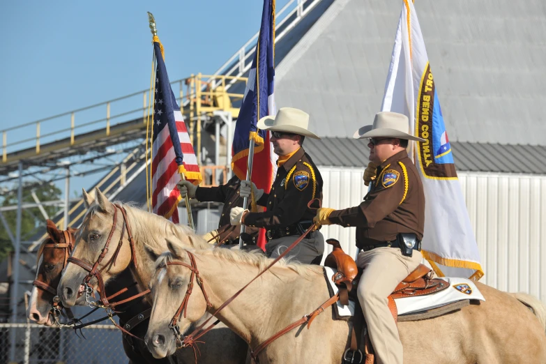 two men in dress clothes on horses holding flags