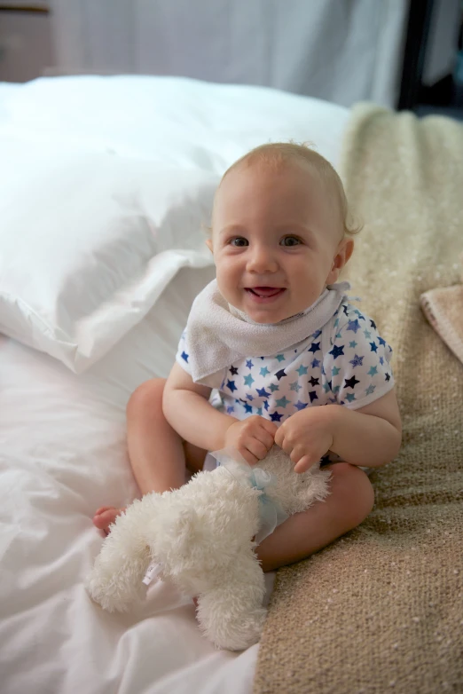 a small baby girl sitting on a bed with her teddy bear