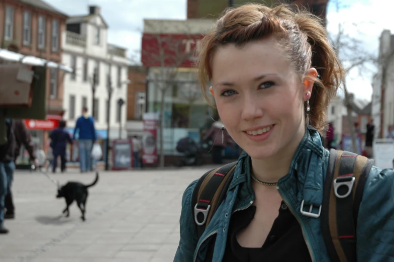 a beautiful woman standing next to a black dog on a sidewalk