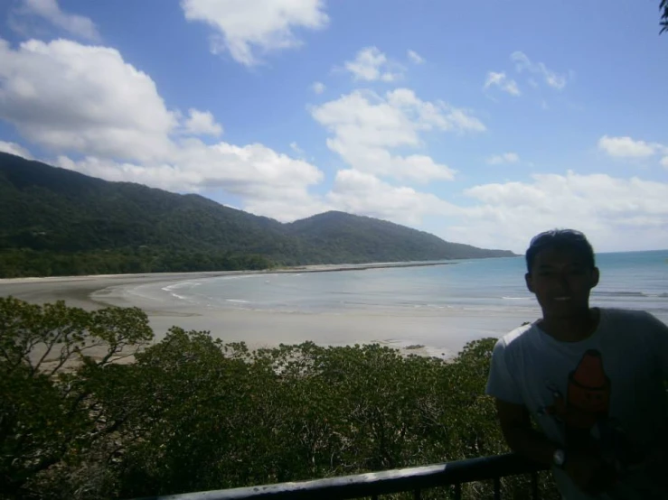 man standing on balcony overlooking sandy beach, mountains and ocean