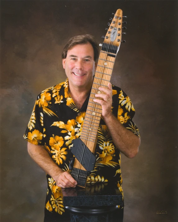 man in hawaiian shirt holding up a brown and yellow guitar