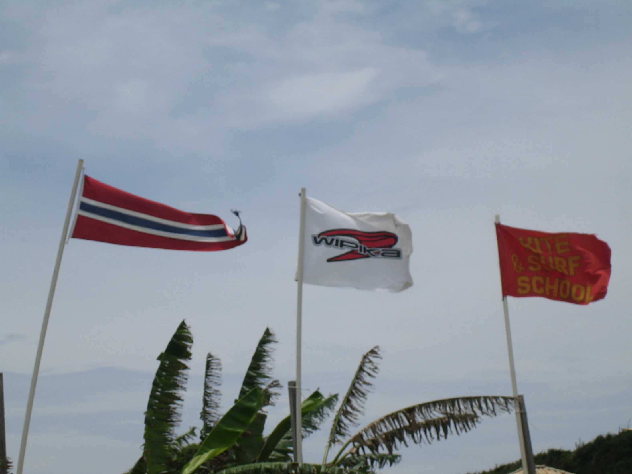 three flags flying high in the air at a beach