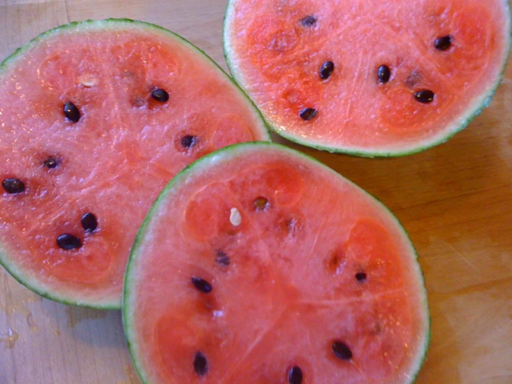 three sliced watermelon on a wooden table with seeds inside