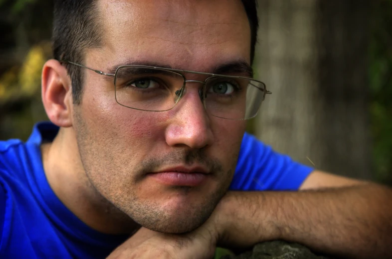 a young man wearing glasses next to a tree