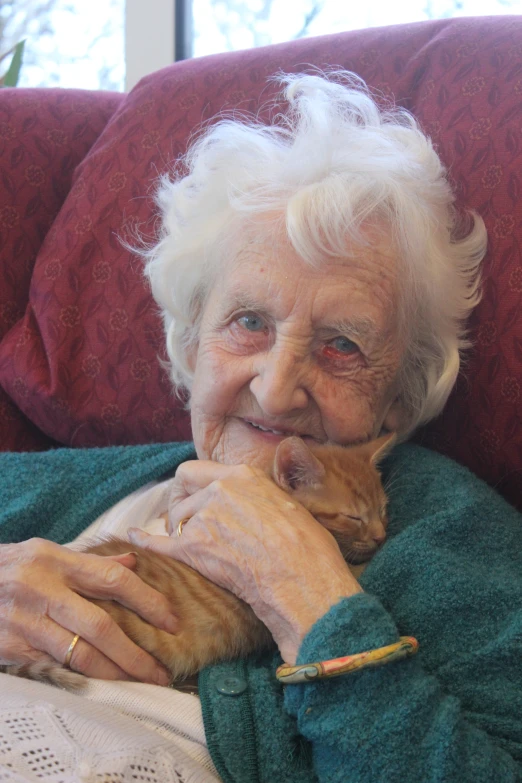 a old woman cuddles her orange cat on a red couch