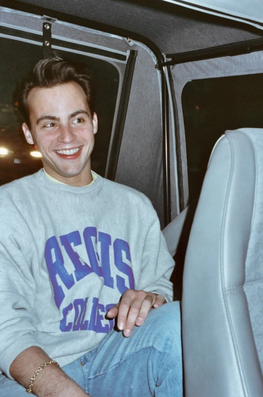 a young man smiles in the back seat of a car