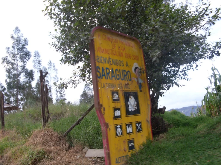 a yellow sign sitting in the grass near a tree