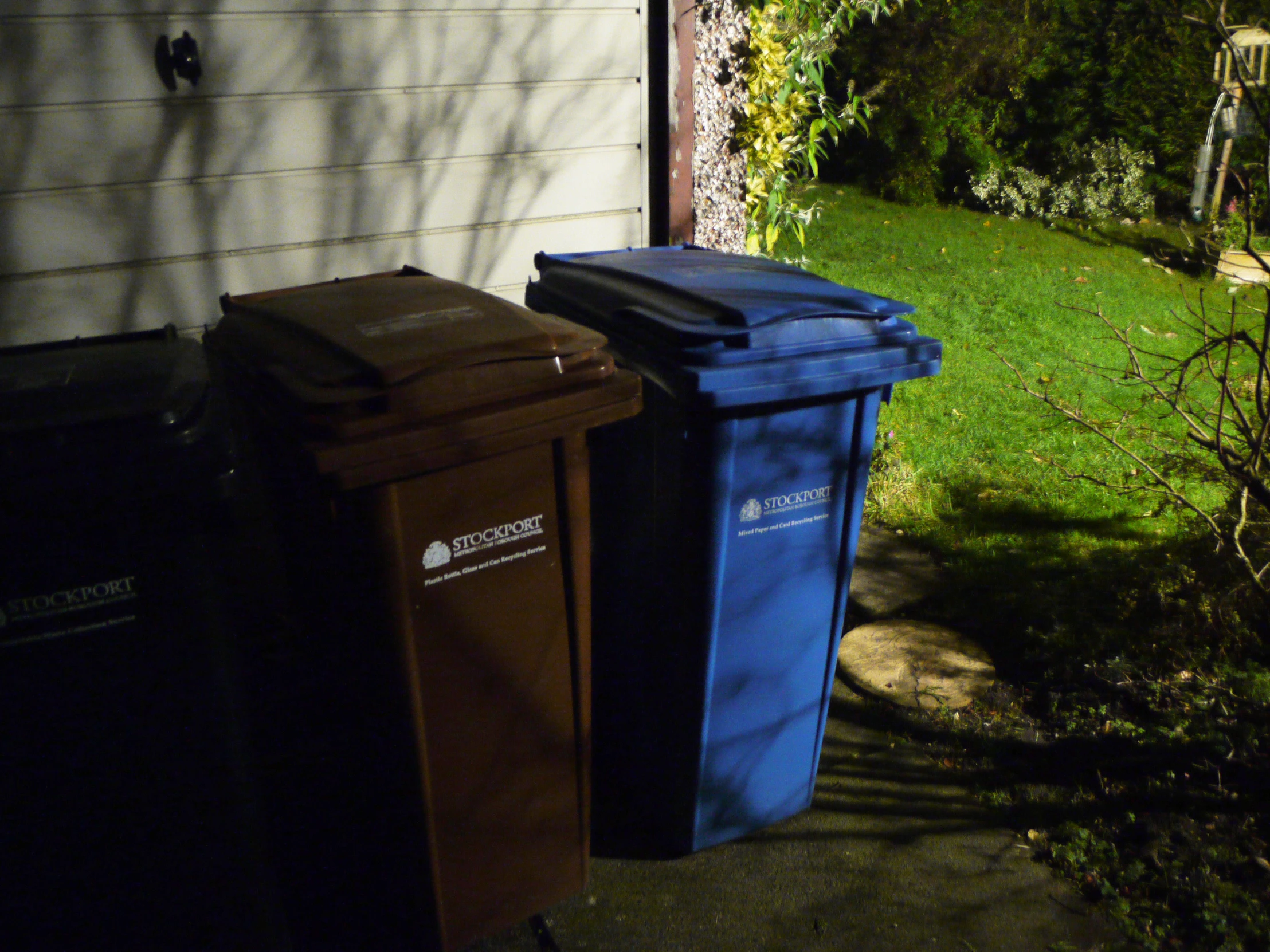 several types of garbage and trash cans on the side of a house