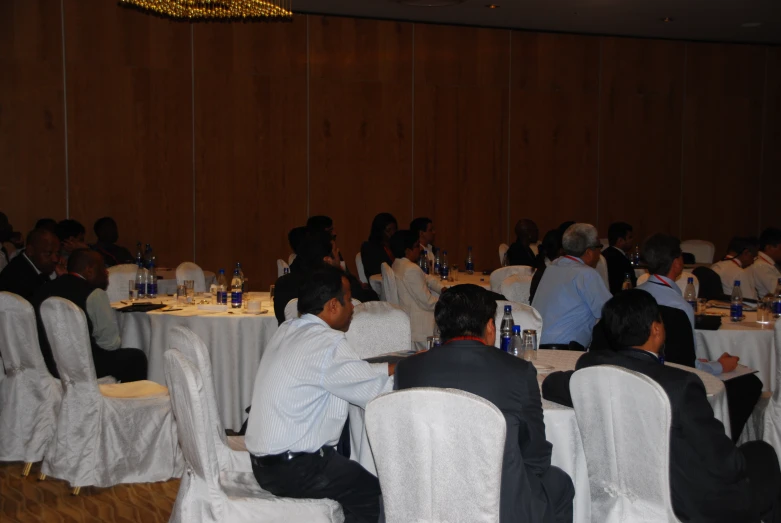 an audience of people are seated in chairs around the tables