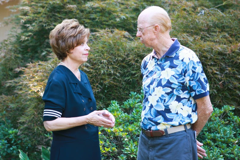 the two people are standing next to each other in front of bushes