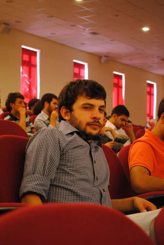 two men sitting in an auditorium with a group of people behind them