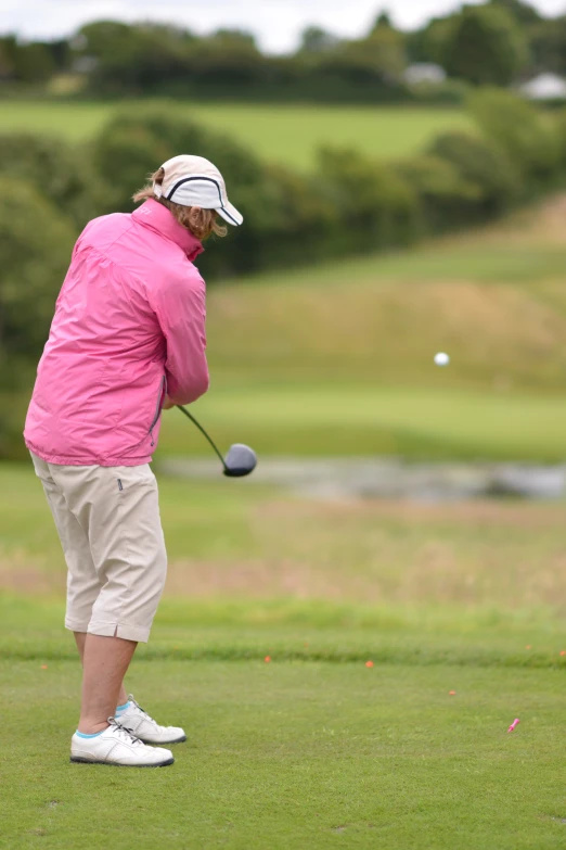 woman in pink jacket playing golf on course at golf club