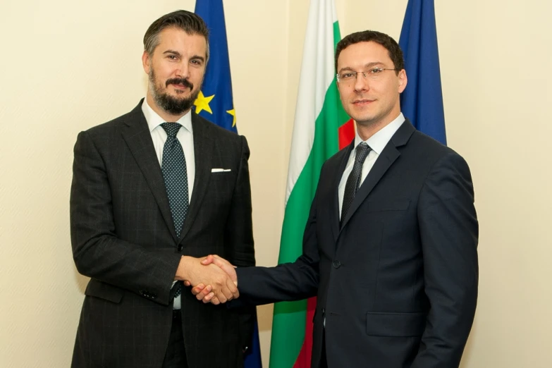 two men in suits are shaking hands with the flags of italy and europe