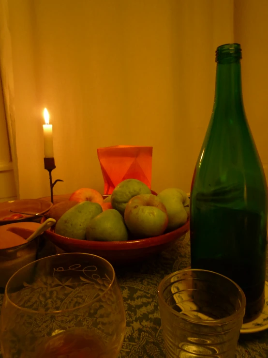 a table topped with a bowl of pears next to a green glass and bottle