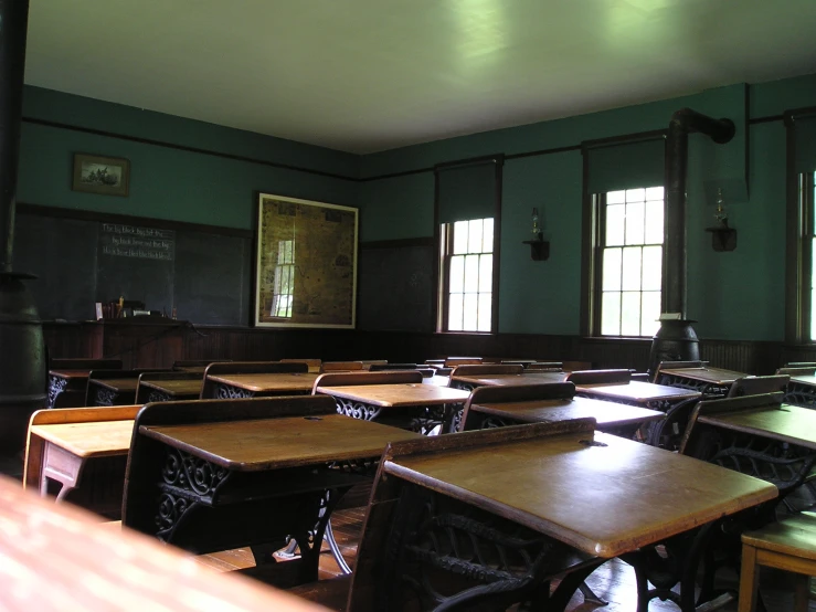 an empty desk in a classroom area in front of three windows