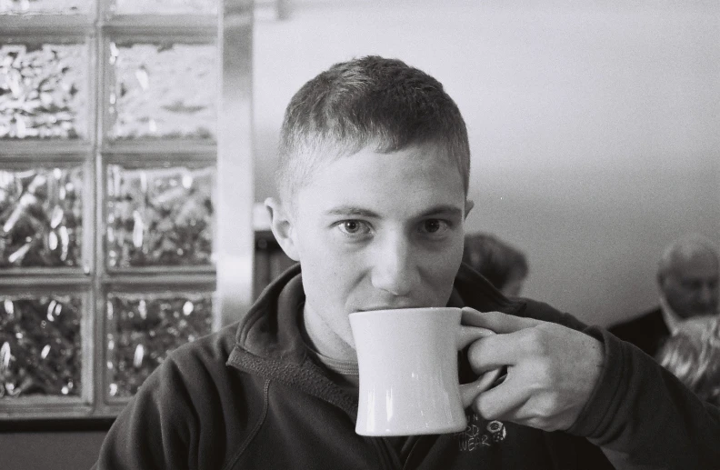 black and white image of a man holding a mug in front of his face