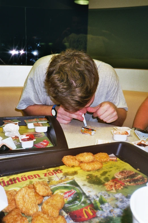 a man in white shirt leaning over a table with trays of food