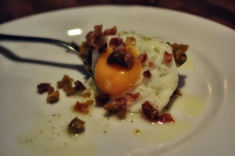 an egg sits on top of bacon on a plate