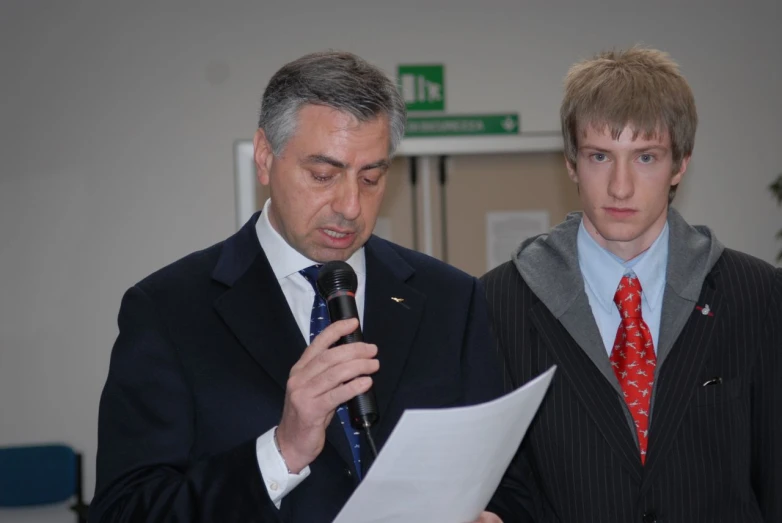 two men standing near each other holding papers